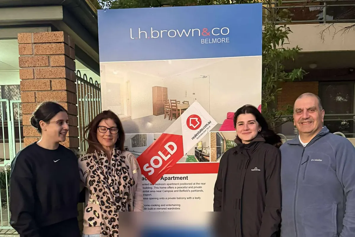 A family in front of the sold sign at the home they bought together