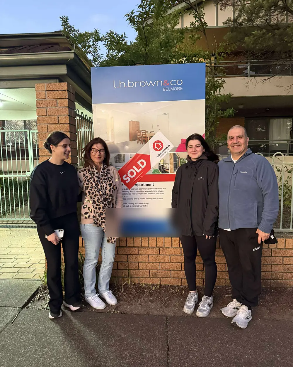 A family in front of the sold sign at the home they bought together