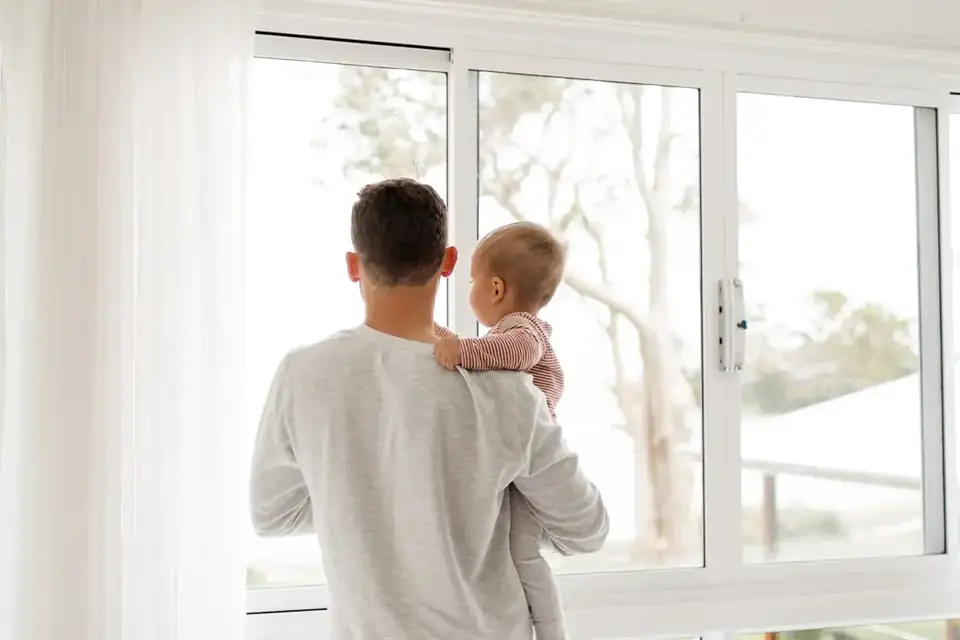A father holding a baby by the window